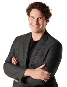 trade show magician Evan Northrup wearing a gray sport coat and black shirt, smiling with arms folded