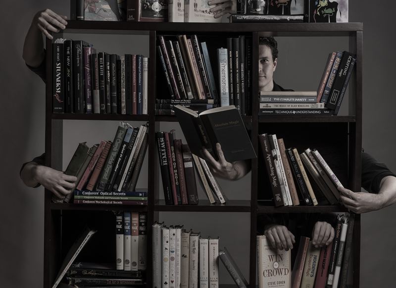 Evan Northrup surrounded by a library of magic and design books
